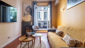 A cozy living room with a sofa, a small round table, a chair, a fireplace, and a balcony with a view.