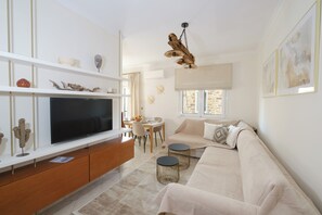 A modern living room with a flat-screen TV, a sofa, a dining table, and a unique wooden ceiling light fixture. - Chios Boho Home (Chios)