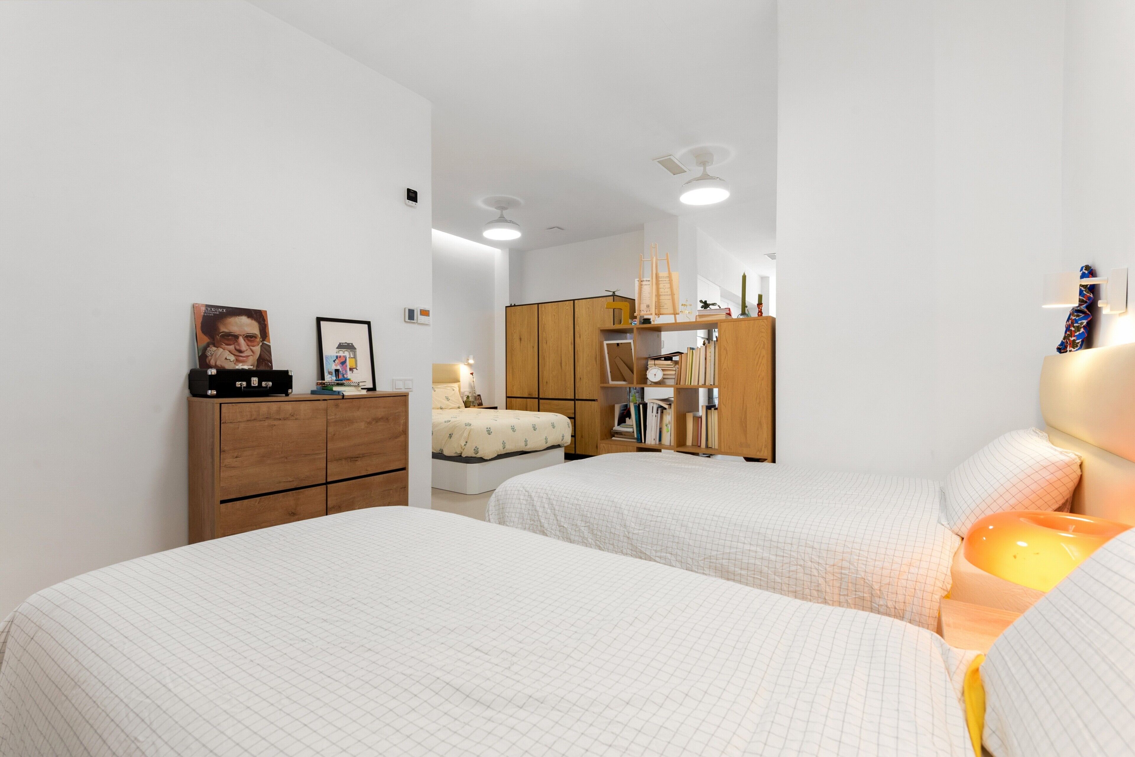 Ein Schlafzimmer mit zwei Betten, einer Holzkommode, einem Bücherregal und einem Schreibtisch mit einer Lampe.
