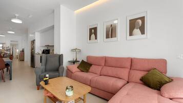 A modern living room with a sofa, a coffee table, and a dining area in the background.