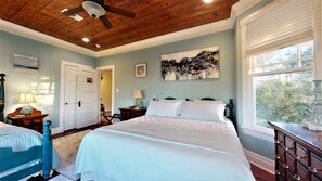 A bedroom with a large bed, a ceiling fan, a window with blinds, and a painting on the wall. - Spirited Garden- Historic/Central to everything (Galveston)