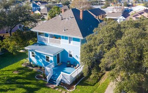 A two-story house with a front porch, a small attached garage, and a backyard. - Spirited Garden- Historic/Central to everything (Galveston)