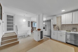 Eine moderne Küche mit weißen Schränken, einem Edelstahlkühlschrank und einer Rückwand mit Fischgrätmuster.