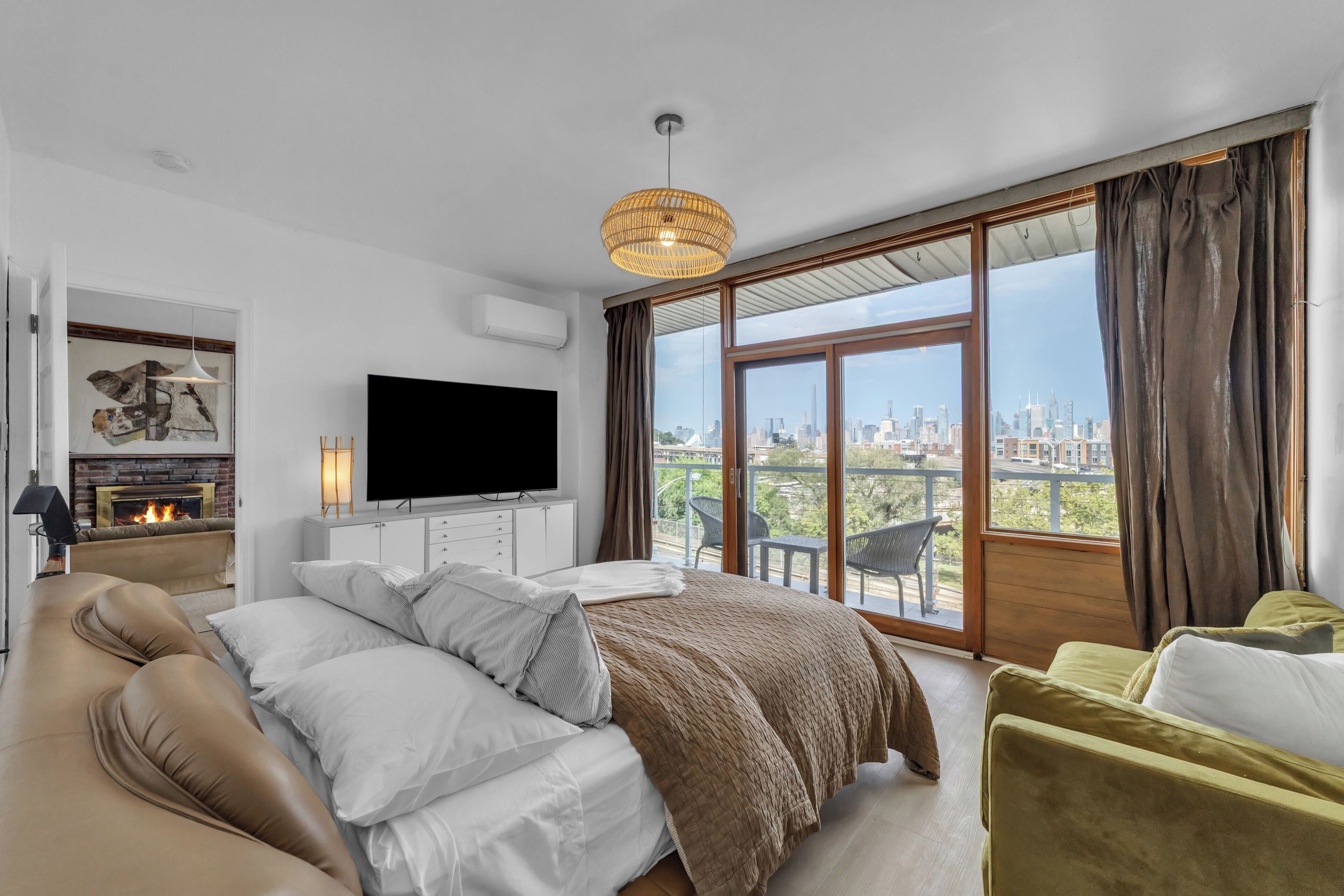 Un dormitorio moderno con una cama grande, un televisor de pantalla plana, una chimenea y vistas a la ciudad a través de amplias ventanas.