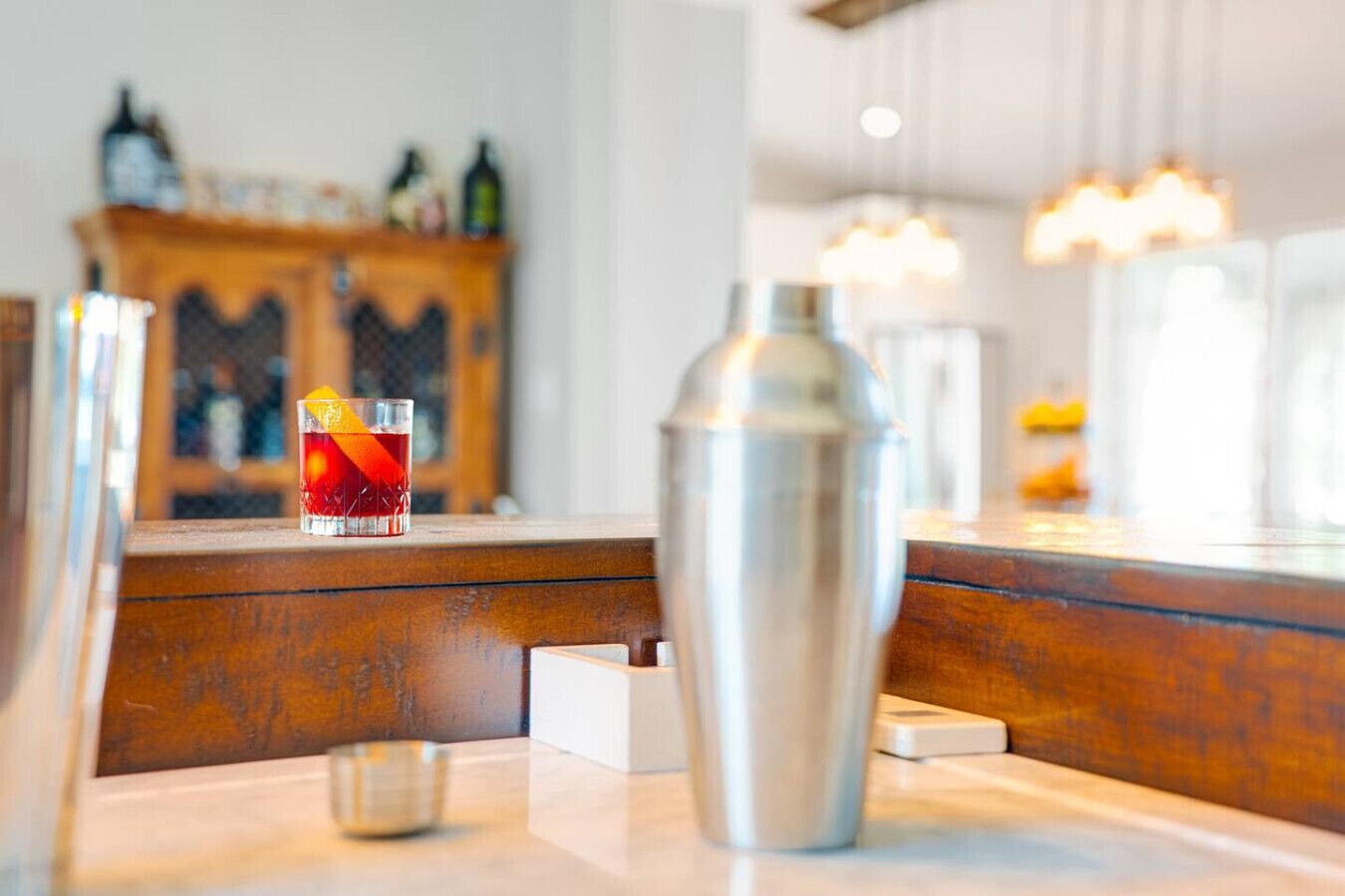 A bar area with a cocktail glass, a metal shaker, and a wooden counter.
