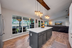 A modern kitchen with large windows, a central island, and a dining area.