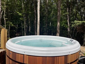 Un jacuzzi en un área boscosa con una terraza de madera y una estructura de madera al fondo.