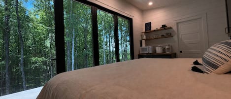 A bedroom with a large bed, a skylight, and a view of a forest through large windows.