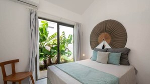 Ein Schlafzimmer mit einem Bett, einem Sessel, einem großen Fenster und einem Wandventilator.