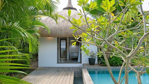 Eine private Villa mit Pool, umgeben von tropischer Vegetation und einem strohgedeckten Gebäude.