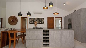 Eine moderne Küche mit Kochinsel, Pendelleuchten und einem Essbereich mit Holzmöbeln.