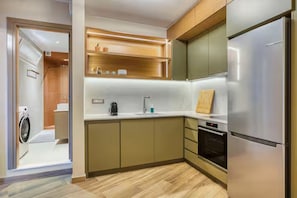 A modern kitchen with built-in appliances, wooden shelves, and a washing machine in the adjacent room. - Chios Comfort Home D1 (Chios)