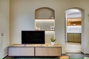 A modern living room with a flat-screen TV on a wooden console, a small plant, and a kitchen visible through an archway. - Chios Comfort Home D1 (Chios)