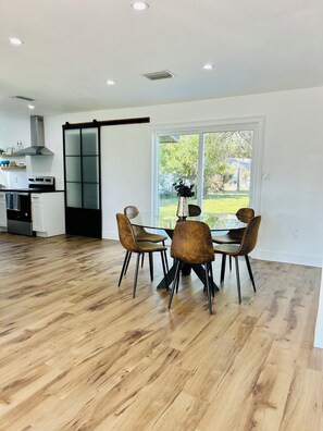 A modern kitchen with a sliding glass door leading to a garden, a dining area with a round table and four chairs, and a wooden floor. - Perfect 2-bedroom house in  charming downtown  Punta Gorda (Punta Gorda)