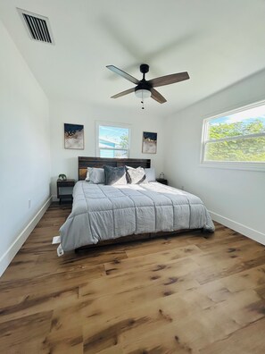 Une chambre à coucher avec un lit, un ventilateur de plafond, une fenêtre et des œuvres d’art accrochées aux murs.