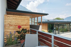 Ein modernes Gebäude mit Holzfassade, einem Balkon mit Metallgeländer und Blick auf Berge.