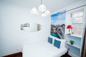 Et soveværelse med en seng, et spejl, et bylandskabsmaleri, en rød lampe og et vindue med udsigt.