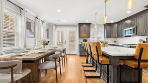 A modern kitchen with wooden flooring, a central island with bar stools, and pendant lighting.