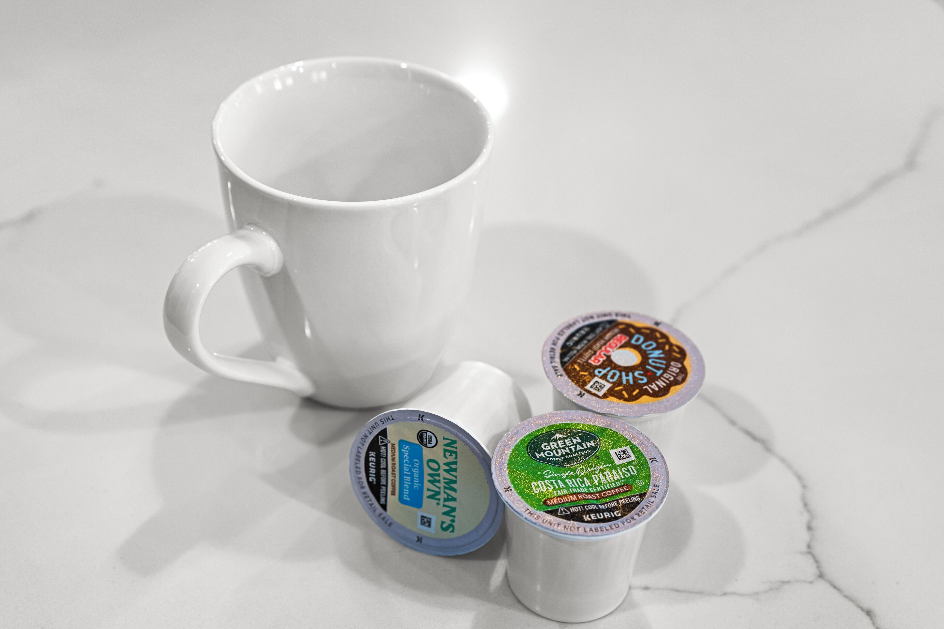 Eine weiße Tasse und drei Kaffeekapseln auf einer Marmorplatte.