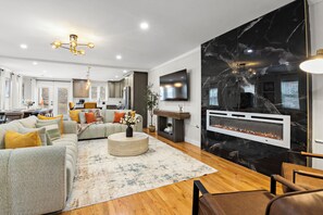 Una sala moderna con un sofá modular, una chimenea, un comedor y una cocina al fondo.