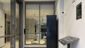 A modern hotel lobby with a glass door entrance, a reception desk, and a sign with emergency procedures. - Think Home Vila Madalena (São Paulo)