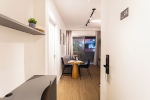 Une chambre d’hôtel moderne avec une table à manger en bois, des chaises noires, une petite plante en pot et un balcon avec vue.