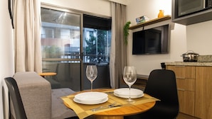 A dining area with a table set for two, a window with curtains, a kitchen area with a microwave, and a plant on the wall. - Think Home Vila Madalena (São Paulo)