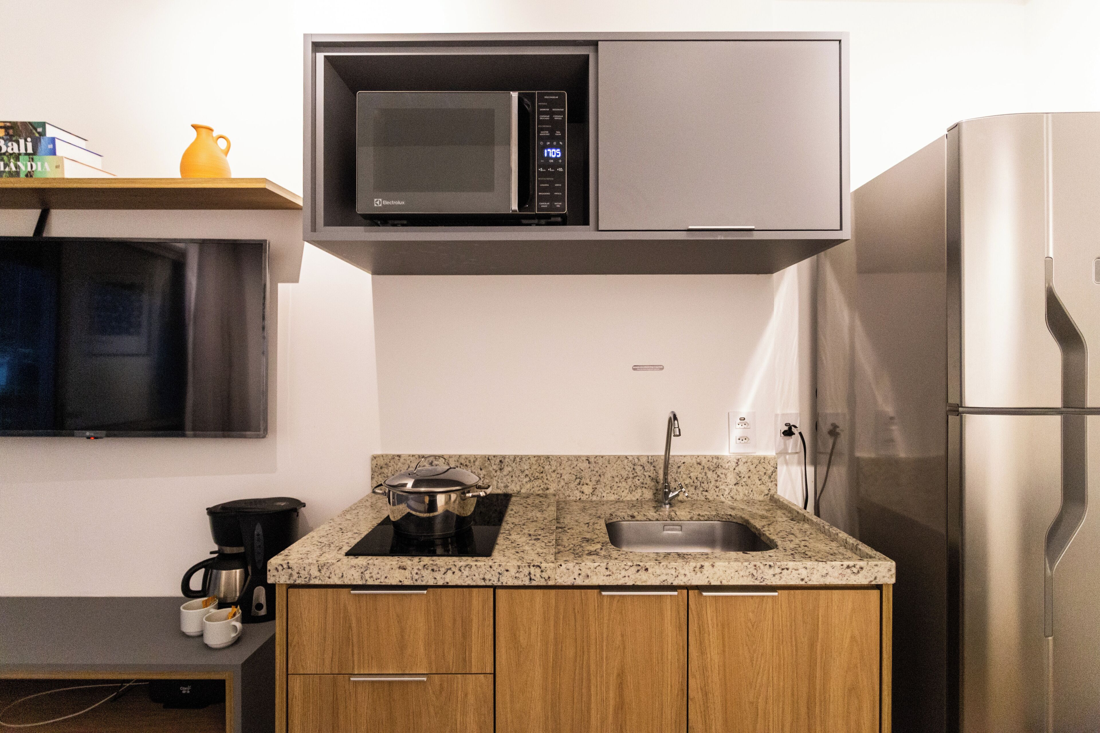 Una cocina compacta con microondas, lavamanos y refrigerador de acero inoxidable.