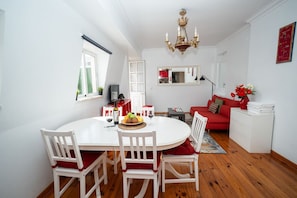 Ein Essbereich mit einem runden Tisch, weißen Stühlen, einer Chandelier und einem roten Sofa.