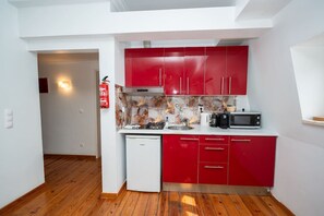 Eine kompakte Küche mit roten Schränken, einer weißen Arbeitsplatte, einer Mikrowelle und einem kleinen Kühlschrank.