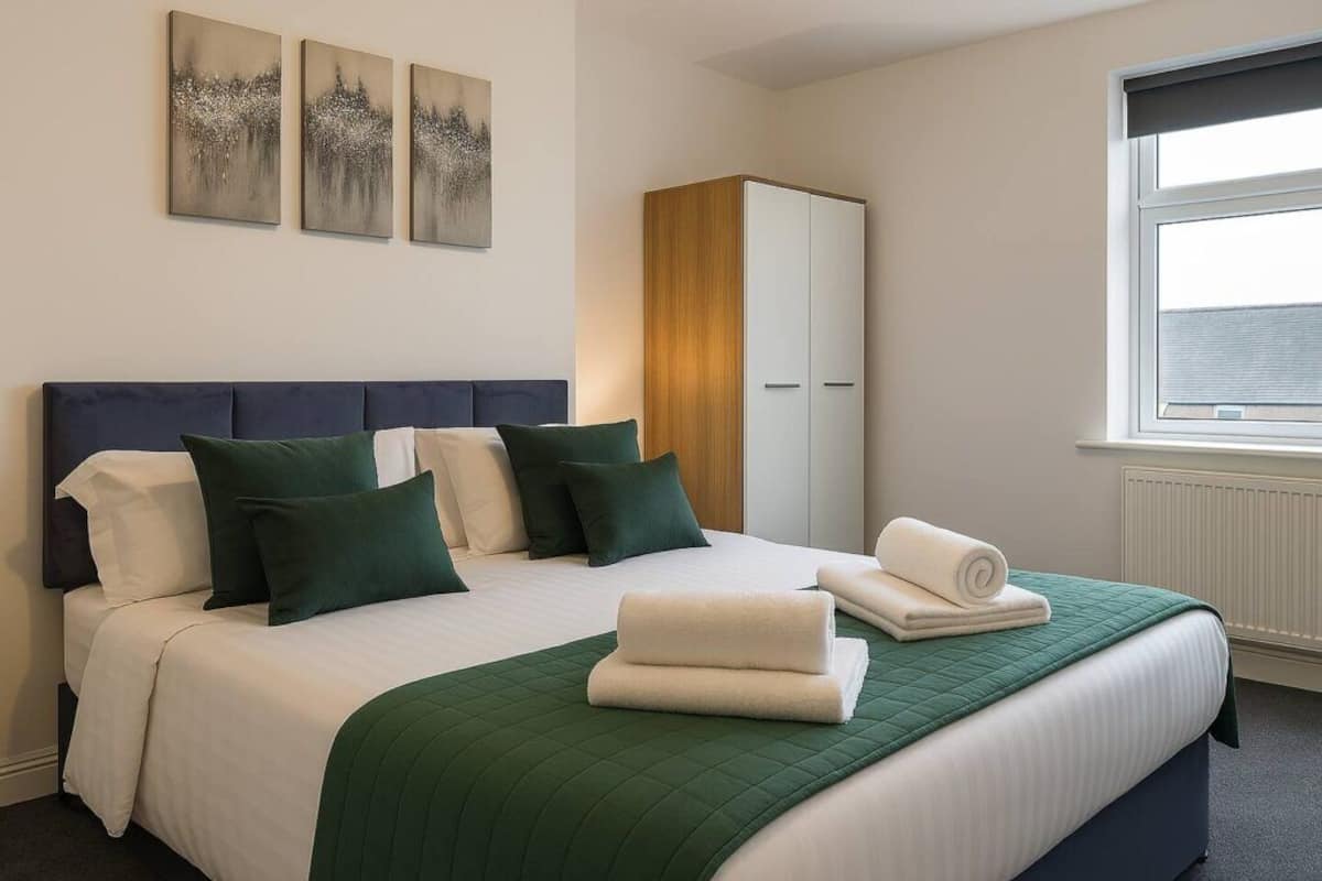 A hotel room with a bed, pillows, a green quilt, a wardrobe, and artwork on the wall.