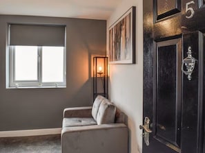 Een kamer met een donkere muur, een raam met jaloezieën, een bank, een deur met een nummer en een lijst met een afbeelding.