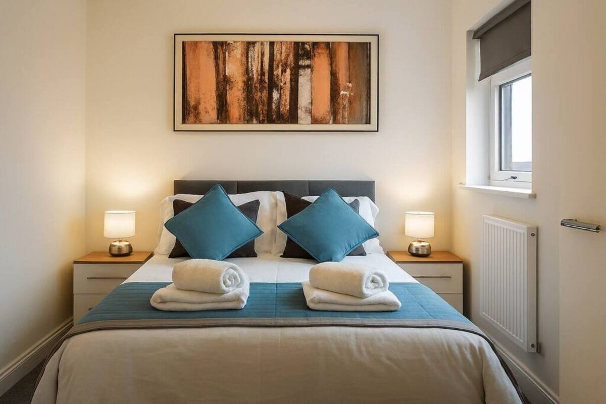 A neatly made bed with two pillows, a bedside lamp, and a rolled towel on the bed.