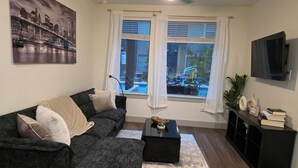A living room with a sofa, a coffee table, a TV, and a window with curtains. - Heart of Addison
In a cozy, friendly and safe community. (Addison)
