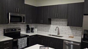 A modern kitchen with dark cabinets, a stainless steel microwave, oven, and dishwasher, a white countertop, and a sign that reads 'THIS MUST BE THE PLACE'. - Heart of Addison
In a cozy, friendly and safe community. (Addison)