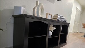 A dark wooden console table with shelves, a framed picture, and books titled 'New York,' 'London,' and 'Paris.' - Heart of Addison
In a cozy, friendly and safe community. (Addison)