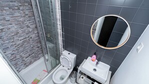 Une salle de bain comprenant des toilettes, un lavabo, un miroir et un espace douche.