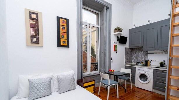 Une petite pièce comprenant un lit, une petite table avec des chaises, un lave-linge et un téléviseur fixé au mur.