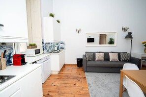 A compact living space with a kitchenette, a gray sofa, a small dining table, and a mirror. - Large 3-Bedroom 2-bathroom 1-Livingroom 2-double bed 2-Twin Bed Apartment (Lisbon)