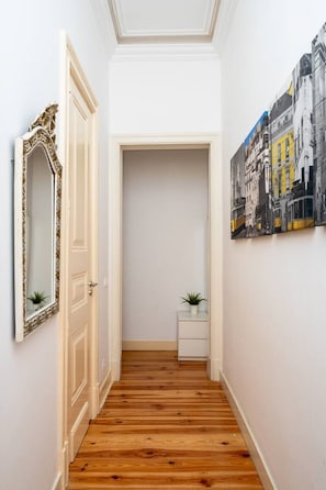Ein Flur mit Holzboden, einer weißen Tür, einem Spiegel, einem kleinen Tisch mit einer Pflanze und einem Stadtbild an der Wand.