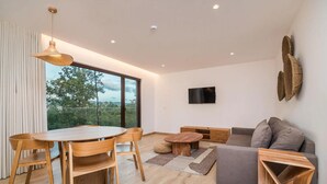 Un salon moderne comprenant un coin repas, un canapé, un téléviseur fixé au mur et une grande fenêtre offrant une belle vue.