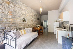 A cozy room with a stone wall, a bed, a dining table, and a kitchenette. - Beachfront Mani Luxury Stone Nest, Steps from Sea (Kokkala)