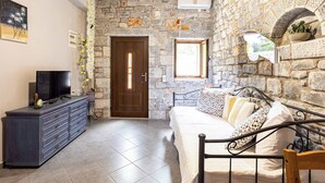 A room with a stone wall, a bed with patterned pillows, a dresser with a TV, and a door with a window. - Beachfront Mani Luxury Stone Nest, Steps from Sea (Kokkala)
