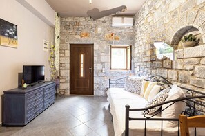 A room with a stone wall, a bed with patterned pillows, a dresser with a TV, and a door with a window. - Beachfront Mani Luxury Stone Nest, Steps from Sea (Kokkala)