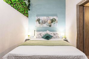 A neatly made bed with a green blanket, a floral pillow, and a wall-mounted artwork above it.