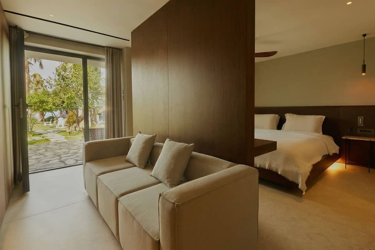 Habitación de hotel moderna con sofá, cama, mesita de noche y vistas al exterior.