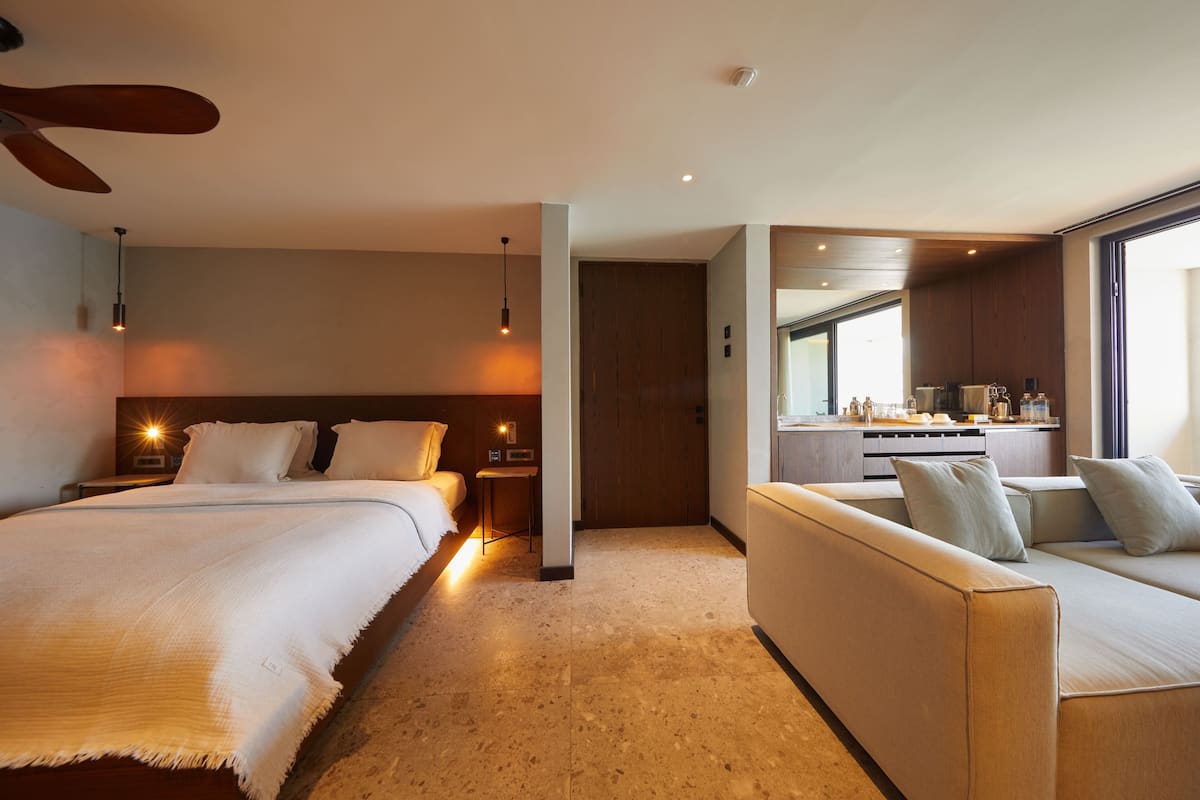 Una habitación de hotel con cama, sofá, una mesita y una kitchenette.
