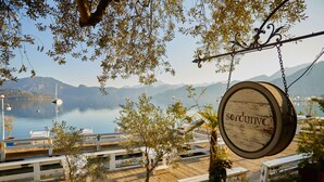 A wooden deck with white railings, a hanging sign with the name 'sardunya,' and a view of a lake with mountains in the background.