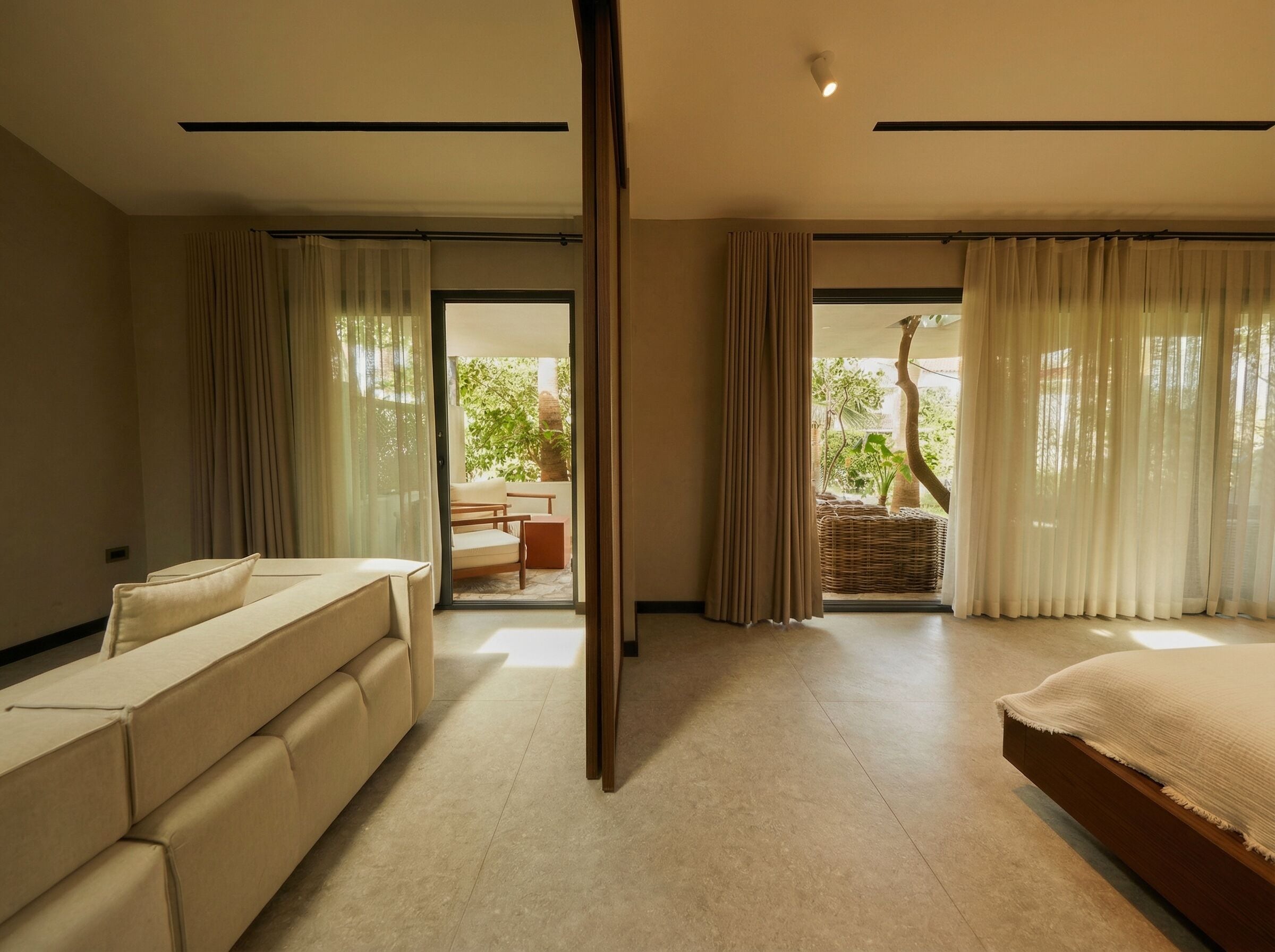 Une chambre d’hôtel moderne, dotée d’un canapé, d’un lit et offrant une vue sur un balcon aménagé avec du mobilier d’extérieur.