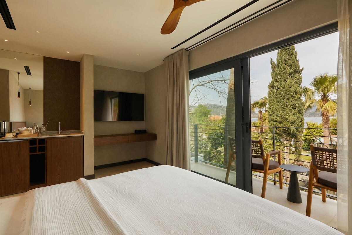 Una habitación de hotel moderna con una cama grande, un televisor, un balcón con asientos y vistas al exterior.